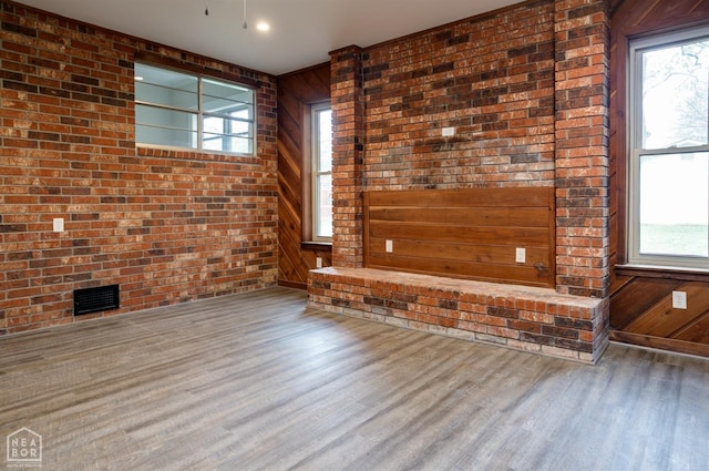 unfurnished living room with brick wall, wooden walls, visible vents, and wood finished floors