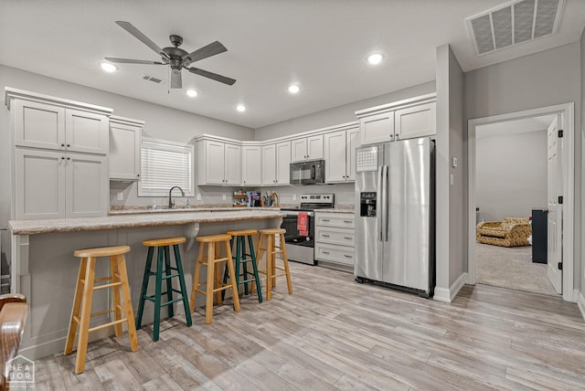 kitchen featuring ceiling fan, visible vents, a breakfast bar, appliances with stainless steel finishes, and light wood finished floors