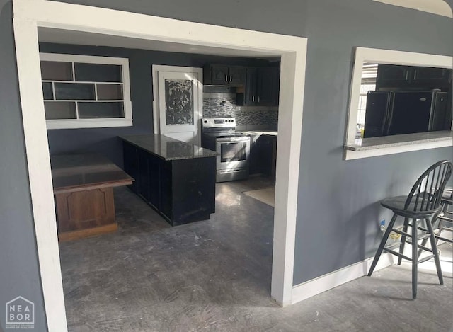 kitchen with dark cabinets, concrete floors, stainless steel range with electric stovetop, decorative backsplash, and baseboards