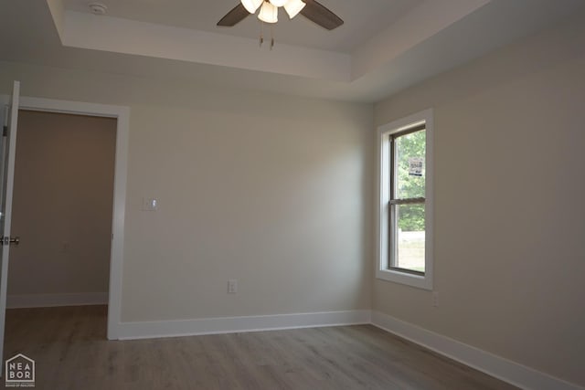 spare room with baseboards, a raised ceiling, ceiling fan, and wood finished floors