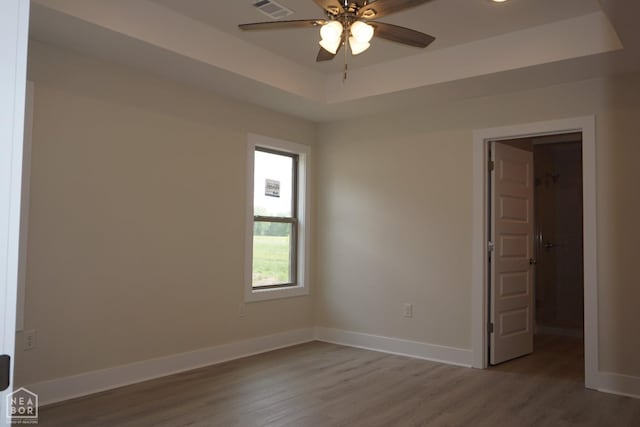 unfurnished room featuring visible vents, wood finished floors, baseboards, ceiling fan, and a tray ceiling