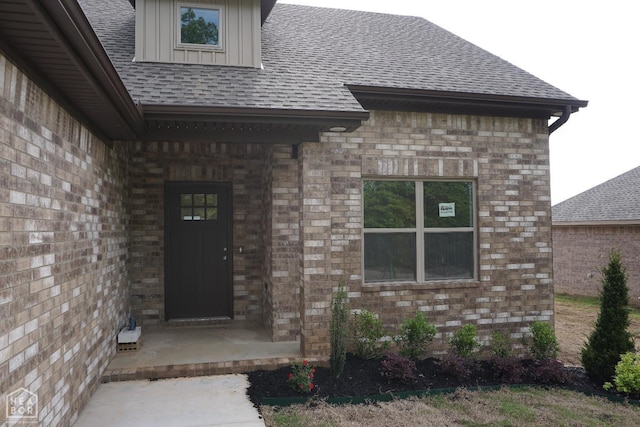 view of exterior entry featuring brick siding and roof with shingles