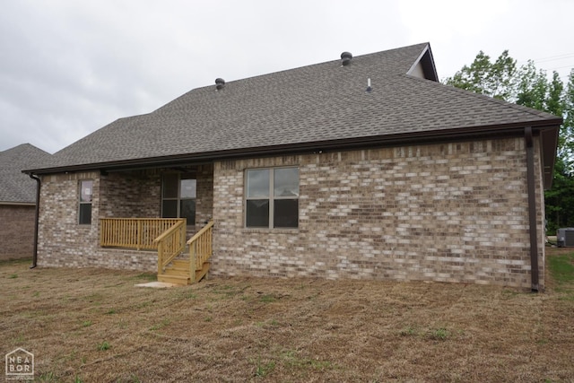 back of property with roof with shingles, central AC unit, a yard, and brick siding