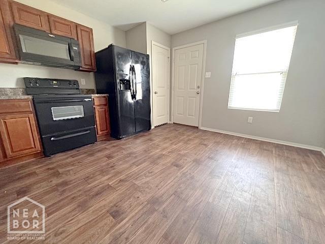 kitchen with black appliances, wood finished floors, brown cabinetry, and baseboards