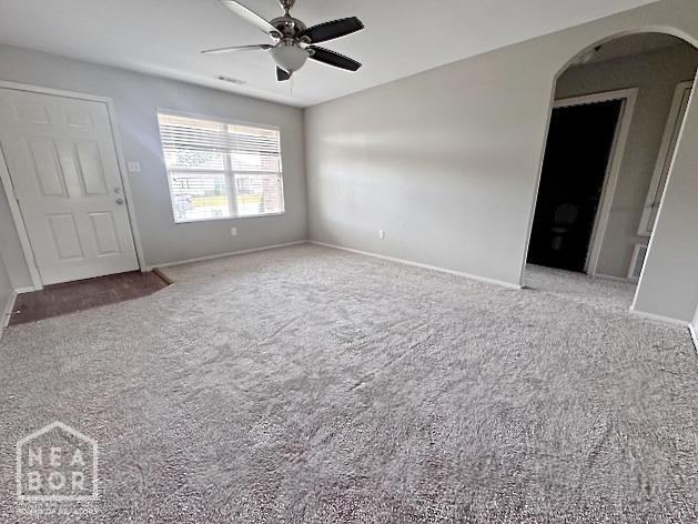carpeted empty room with arched walkways, a ceiling fan, and baseboards