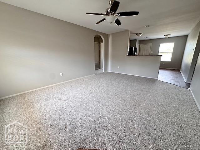 unfurnished living room with ceiling fan, baseboards, and arched walkways