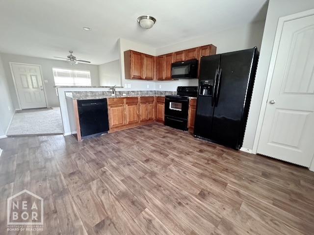 kitchen featuring black appliances, wood finished floors, a ceiling fan, light countertops, and brown cabinetry
