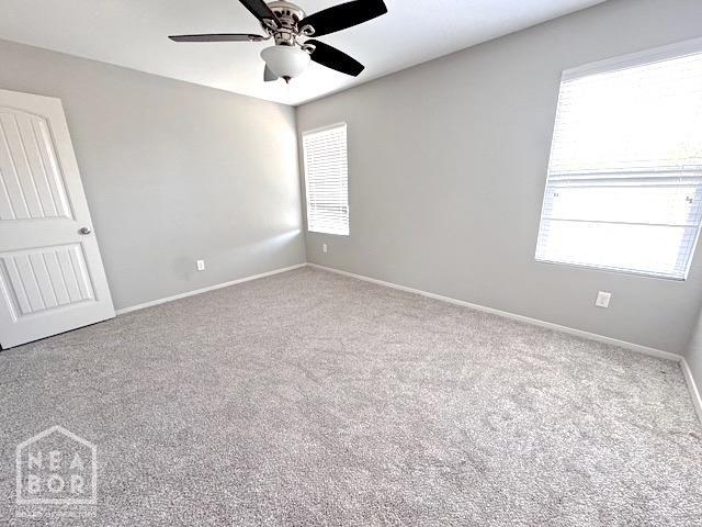 carpeted empty room featuring healthy amount of natural light, a ceiling fan, and baseboards