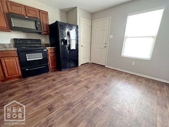 kitchen with black appliances, dark wood finished floors, brown cabinets, and baseboards