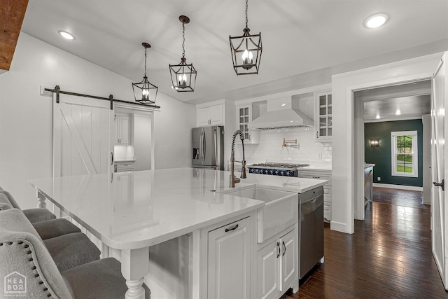 kitchen featuring custom exhaust hood, white cabinets, a barn door, stainless steel appliances, and decorative backsplash