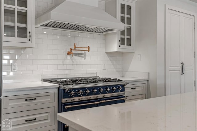 kitchen featuring custom exhaust hood, tasteful backsplash, glass insert cabinets, white cabinets, and high end black range oven