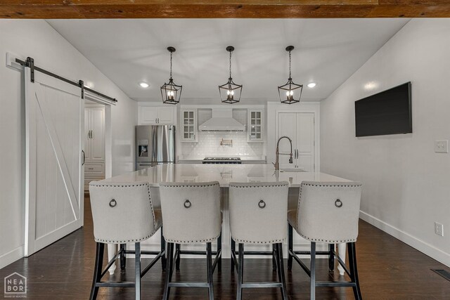 kitchen with wall chimney exhaust hood, tasteful backsplash, a barn door, stainless steel fridge, and baseboards