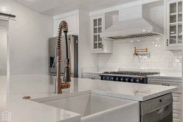 kitchen featuring tasteful backsplash, wall chimney range hood, appliances with stainless steel finishes, and white cabinetry