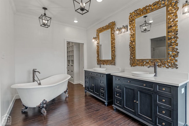 full bathroom with a freestanding bath, a sink, ornamental molding, wood finished floors, and two vanities