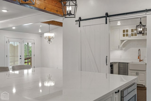 kitchen with tasteful backsplash, light stone counters, white cabinets, a barn door, and a sink