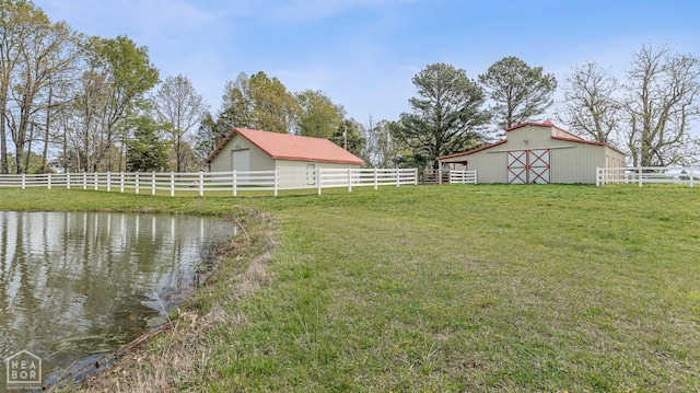 view of yard featuring a barn, a water view, fence, and an outbuilding