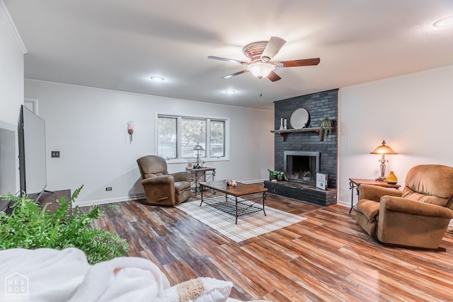 living room with baseboards, ornamental molding, ceiling fan, wood finished floors, and a fireplace