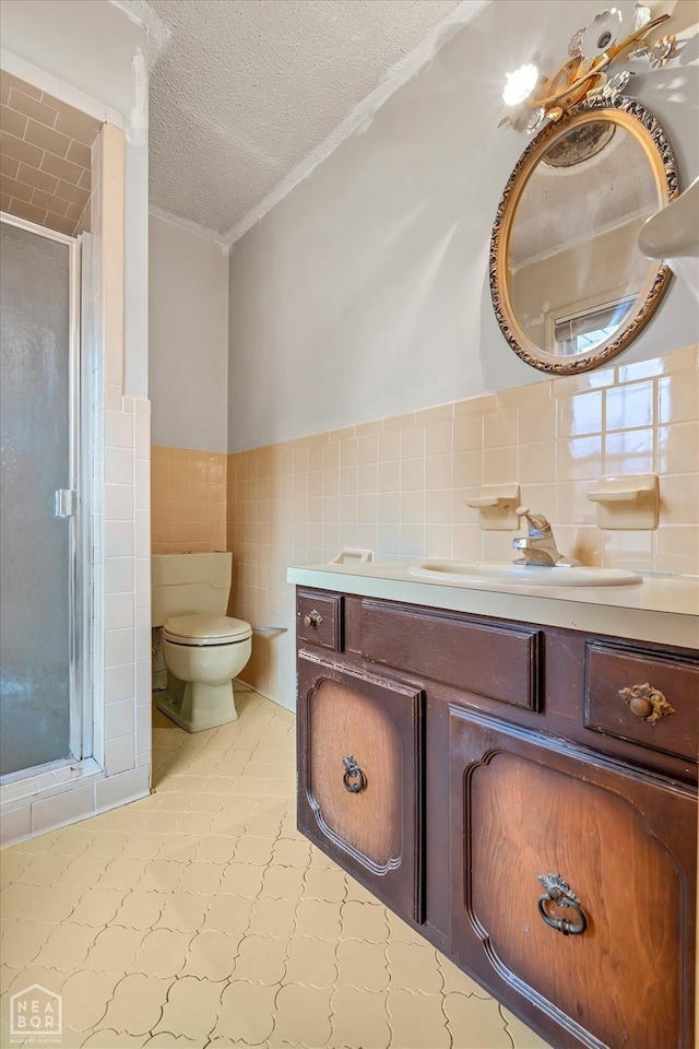full bathroom with vanity, a stall shower, a textured ceiling, toilet, and tile walls