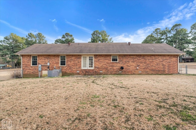back of property with central air condition unit, a lawn, roof with shingles, fence, and brick siding