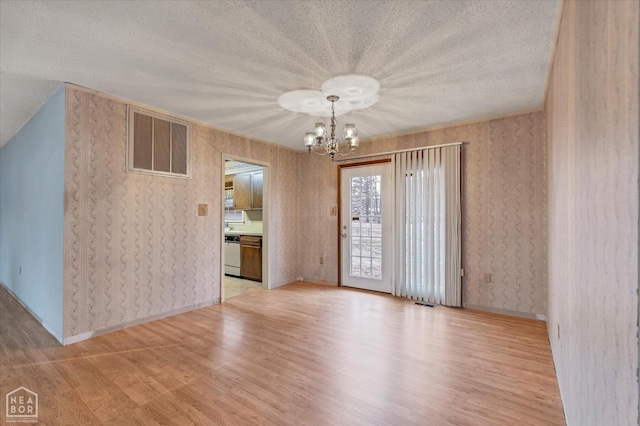 empty room featuring visible vents, a textured ceiling, an inviting chandelier, and wood finished floors
