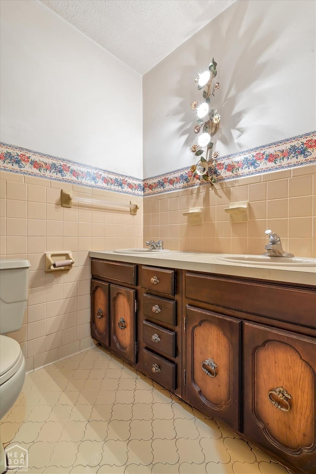 bathroom with tile walls, toilet, a textured ceiling, vanity, and a wainscoted wall