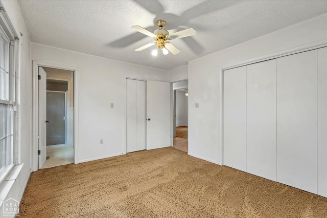 unfurnished bedroom featuring ceiling fan, ensuite bathroom, a textured ceiling, carpet flooring, and multiple closets