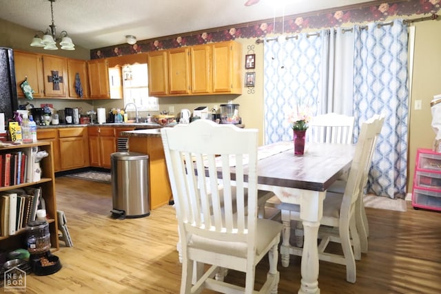 kitchen with a peninsula, light wood-type flooring, a sink, a notable chandelier, and hanging light fixtures