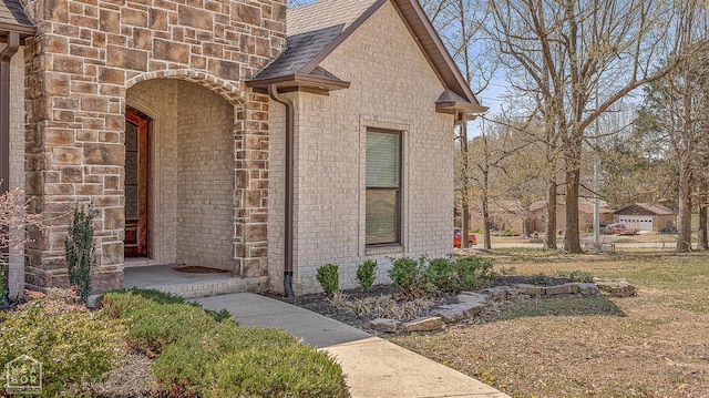 entrance to property featuring brick siding and roof with shingles