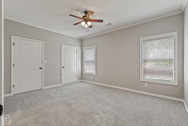 carpeted empty room with crown molding, visible vents, baseboards, and ceiling fan