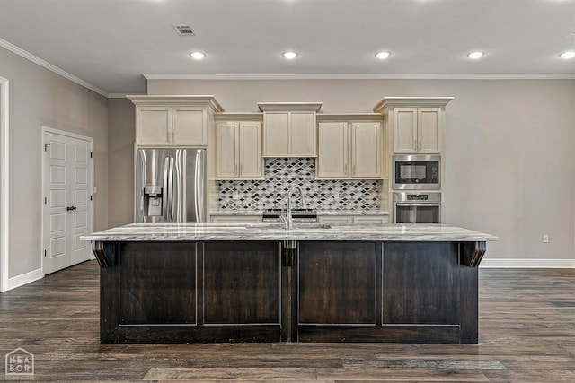 kitchen with cream cabinets, an island with sink, light stone countertops, baseboards, and appliances with stainless steel finishes