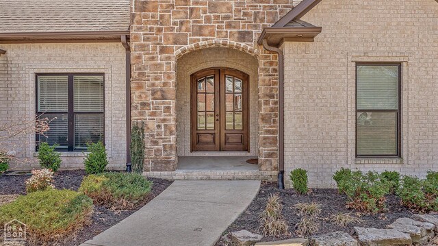 entrance to property featuring brick siding, roof with shingles, and french doors