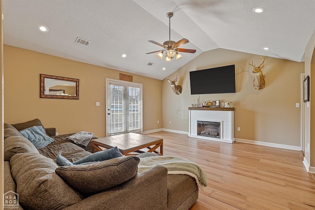living room with a fireplace, light wood-style floors, a ceiling fan, lofted ceiling, and visible vents