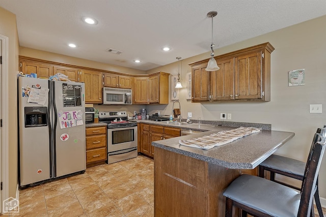 kitchen with stainless steel appliances, brown cabinetry, a sink, and a peninsula