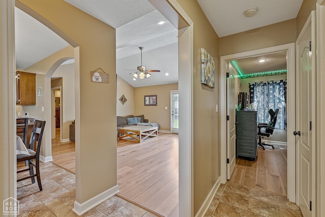 corridor with baseboards, arched walkways, light wood-style floors, and lofted ceiling