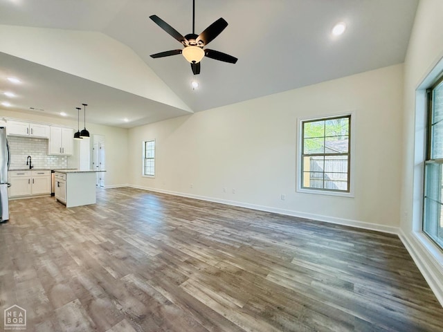 unfurnished living room featuring a wealth of natural light, ceiling fan, wood finished floors, and lofted ceiling