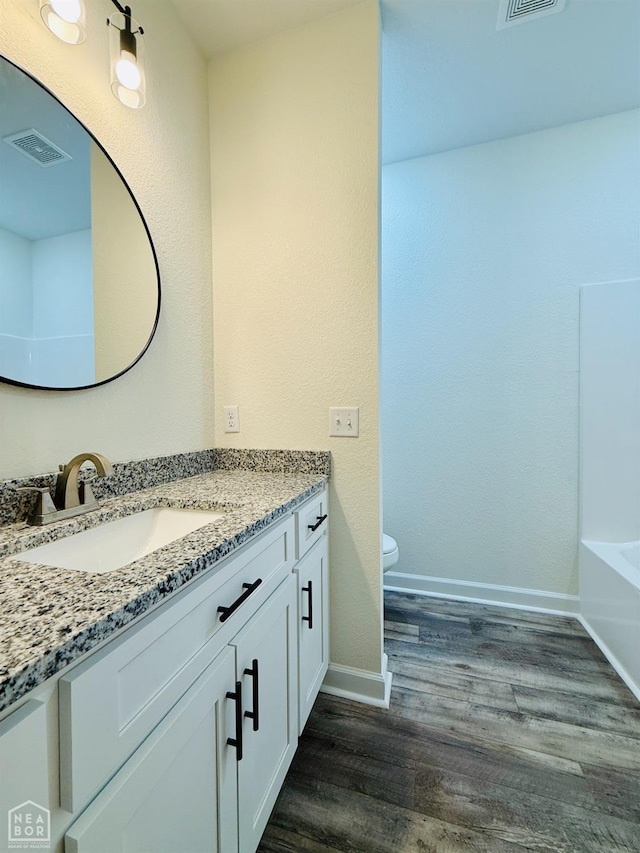 bathroom with vanity, a bathtub, toilet, visible vents, and wood finished floors