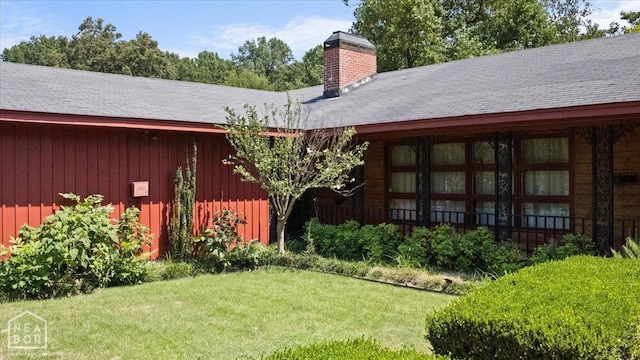 rear view of property with board and batten siding, a lawn, and a chimney
