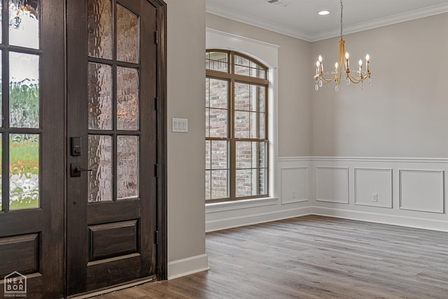 foyer entrance featuring visible vents, an inviting chandelier, a decorative wall, ornamental molding, and wood finished floors