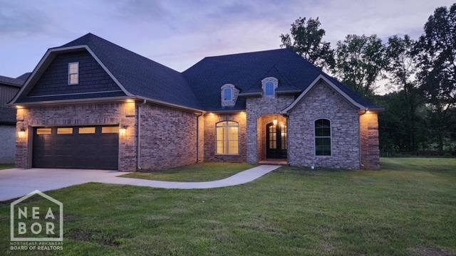 french country inspired facade with an attached garage, driveway, stone siding, and a lawn