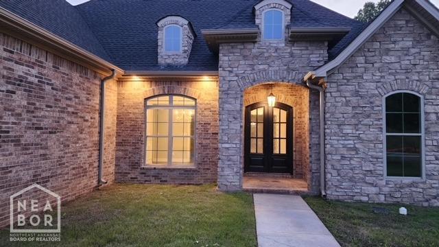 view of exterior entry with french doors, stone siding, and a lawn