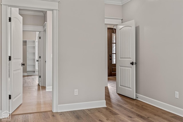 unfurnished bedroom featuring crown molding, a closet, baseboards, and wood finished floors