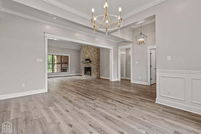 unfurnished living room with crown molding, a stone fireplace, a notable chandelier, and wood finished floors