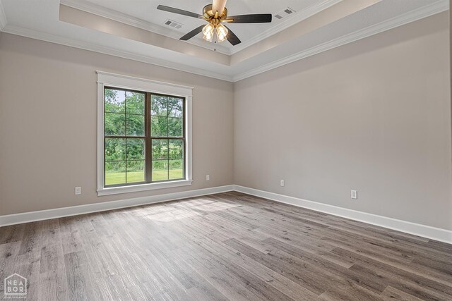 empty room featuring a tray ceiling, ornamental molding, and wood finished floors