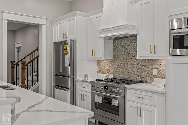 kitchen featuring tasteful backsplash, premium range hood, white cabinetry, light stone countertops, and stainless steel appliances