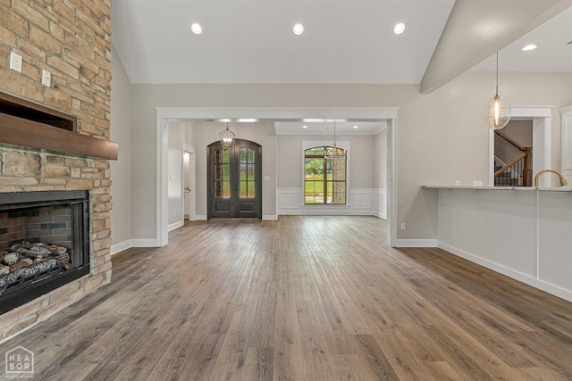 unfurnished living room featuring a fireplace, stairway, wood finished floors, vaulted ceiling, and french doors