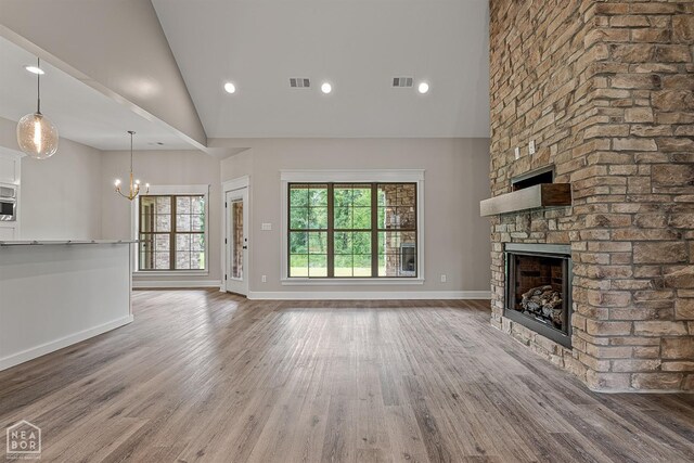 unfurnished living room with a fireplace, visible vents, a chandelier, wood finished floors, and baseboards