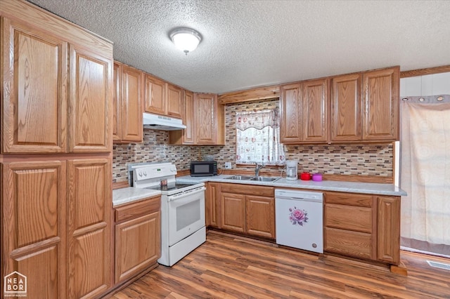 kitchen with a sink, a textured ceiling, white appliances, light countertops, and under cabinet range hood