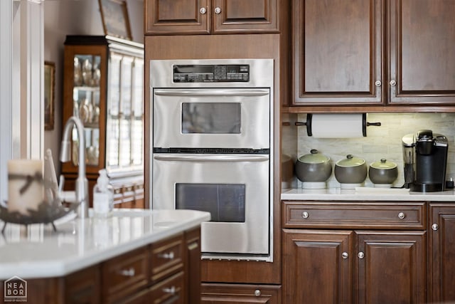 kitchen featuring stainless steel double oven, tasteful backsplash, light countertops, and dark brown cabinets