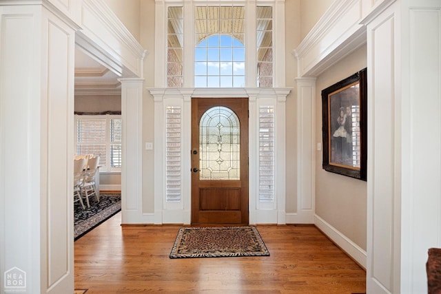 foyer entrance featuring decorative columns, light wood finished floors, baseboards, and ornamental molding