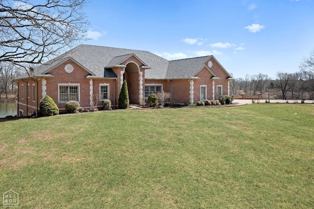 view of front of home featuring roof with shingles, a front yard, and brick siding